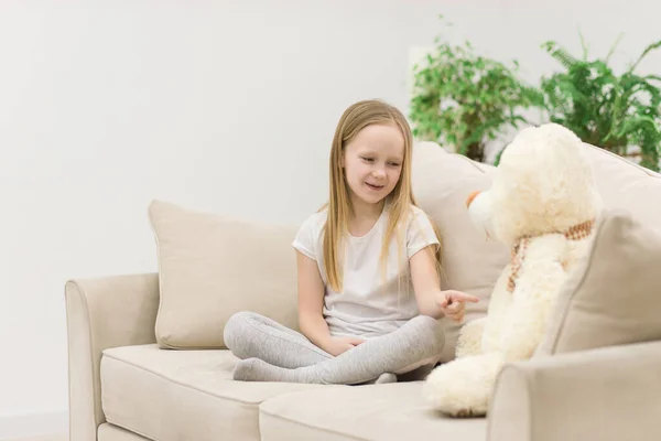 Фото маленької дівчинки, що грає на білому дивані з плюшевим ведмедем . — стокове фото
