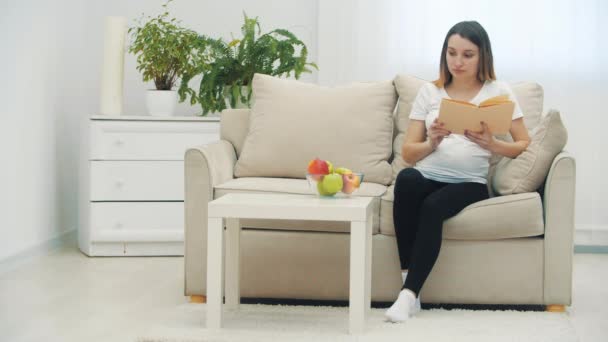 4k видео беременной женщины, читающей книгу и держащей яблоко. — стоковое видео