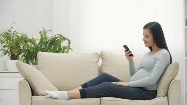 4k lassított felvétel terhes nő ül a fehér kanapén, és mutatja hüvelykujját felfelé. — Stock videók