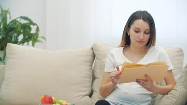 4k video de la mujer embarazada leyendo un libro y sosteniendo una manzana. — Vídeo de stock