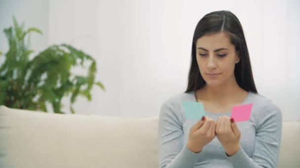 Vidéo 4k de la femme enceinte tenant des papiers roses et bleus qui signifient le sexe du futur bébé. — Video