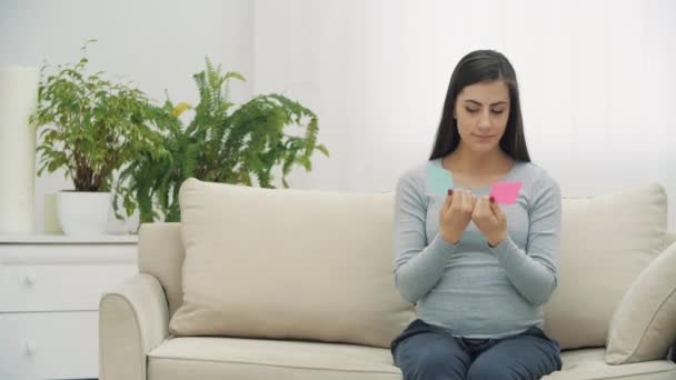 4k видео беременной женщины с розовыми и голубыми бумагами, которые означают пол будущего ребенка. — стоковое видео