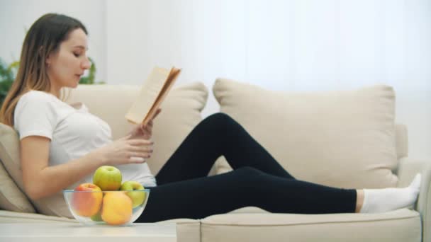 4k-Video einer schwangeren Frau, die ein Buch liest und einen Apfel isst. — Stockvideo