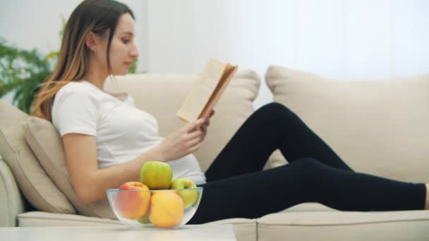 4k wideo ciężarnej kobiety czytającej książkę i jedzącej jabłko. — Wideo stockowe