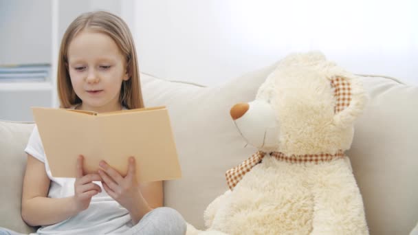 4k slowmotion video of little girl reading a book to her teddy bear. — Stock Video