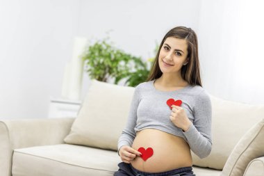 Elinde kırmızı bir kalp tutan hamile kadının fotoğrafı..