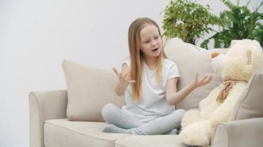 Beyaz elbiseli küçük bir kızın oyuncak ayıya bir şey anlattığı 4K video..