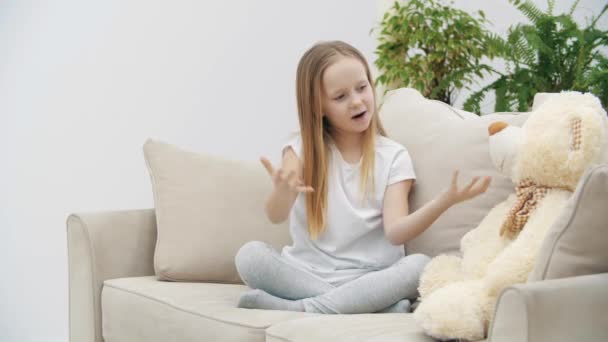 Vidéo 4k de petite fille en vêtements blancs décrivant quelque chose à ours en peluche. — Video