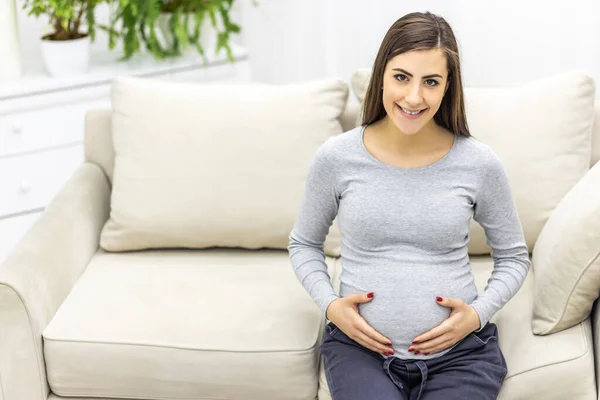 Foto einer schwangeren Frau, die in die Kamera schaut und ihren Bauch berührt. — Stockfoto