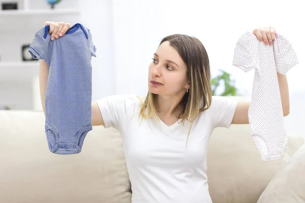 Foto de mulher grávida segurando duas roupas de criança. — Fotografia de Stock