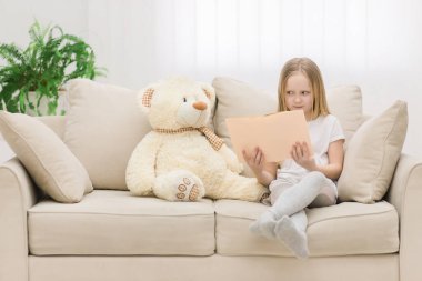 Pelüş oyuncak ayı ve küçük kızın bir kitap tutarken çekilmiş fotoğrafı..