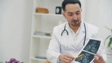Doktorun beyaz önlük giyip ultrason fotoğraflarını tutarken ve açıklama yaparken 4K videosu..
