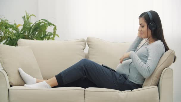 4k videó terhes nő fejhallgató a gyomorban. — Stock videók