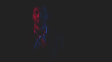 Siyah arka planda mavi ve pembe ışıklarla poz veren takım elbiseli bir adamın 4k videosu..