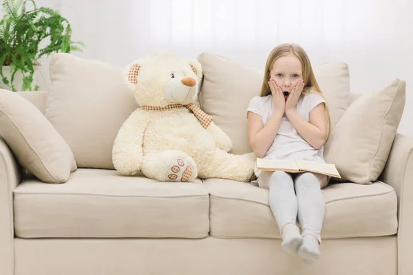 Обрізана фотографія здивованої маленької дівчинки, яка торкається її обличчя руками біля плюшевого ведмедя . — стокове фото