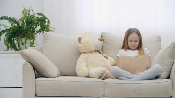 4k відео здивованої маленької дівчинки торкається її обличчя руками біля плюшевого ведмедя . — стокове відео
