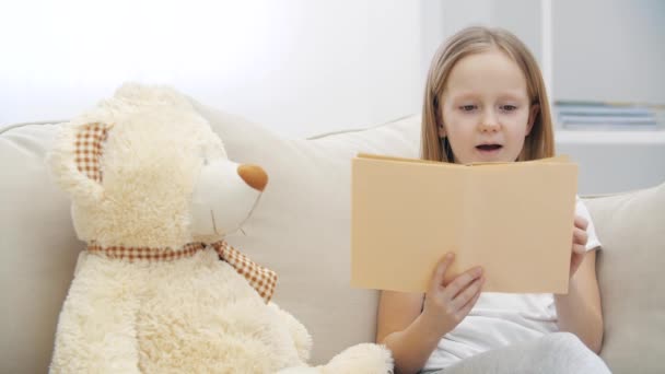 Vidéo 4k de petite fille lisant un livre à son ours en peluche. — Video