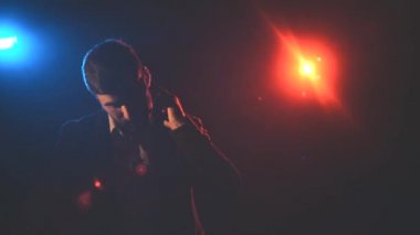 4k video of man in suit sending air kiss on black background with blue and pink lights.