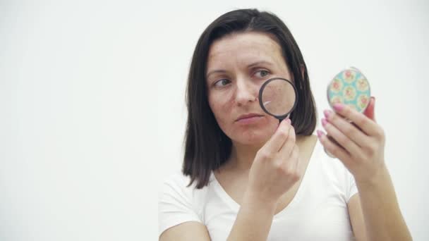 4k video of woman with bad skin looking through magnifying glass and holding mirror. — ストック動画