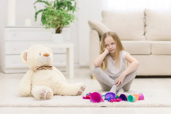 Foto de niña triste sentada en el suelo con juguetes. —  Fotos de Stock