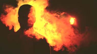 Arka planda gölgeli, dumanlı ve turuncu ışıklı bir adam videosu var..