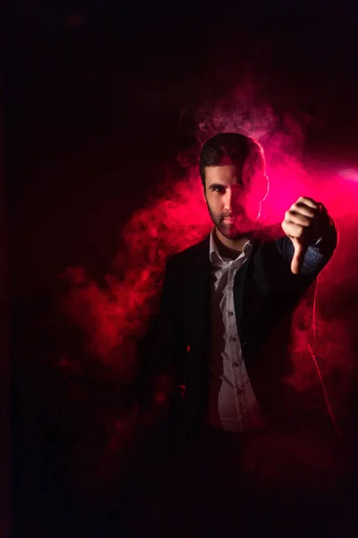親指を示すピンクの煙の中でスーツを着た男の写真 親指を示す男の概念 ロイヤリティフリーのストック画像