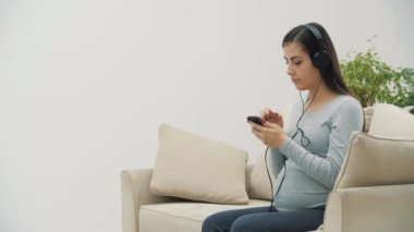 Hamile bir kadının müzik dinlerken 4K yavaş çekim videosu. Kulaklıklı hamile kadın kavramı.