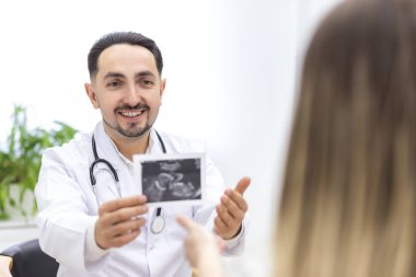 Doktorun laboratuvar önlüğü giymiş bir fotoğrafı hastasına ultrason sonuçlarını gösteriyor. Sağlık hizmetleri kavramı.