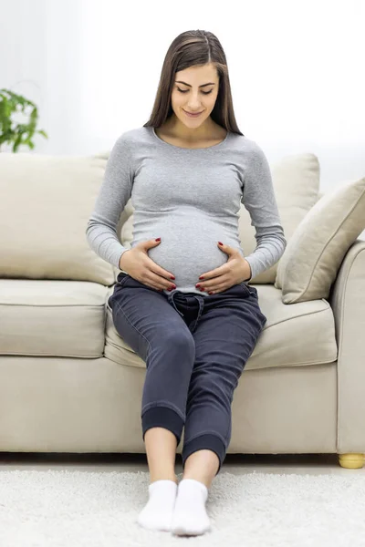 Photo Pregnant Woman Hugging Her Stomach Couch Living Room Concept — Stockfoto