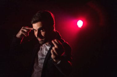 Orta parmağını şakağına dayayan ve arka planda pembe ışığı olan ayakta duran adamın fotoğrafı. Takım elbiseli adam kavramı.