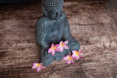 Koyu arkaplanda Frangipani çiçekleri olan Buda heykeli