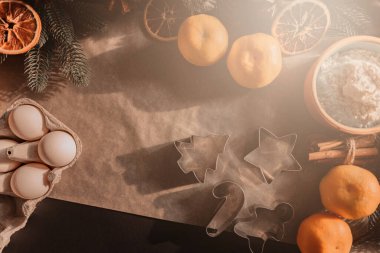 2021 yılının şenlikli arka planı. Koyu arkaplanda ve parşömende ev yapımı Noel kurabiyeleri pişirmek için gerekli malzemeler