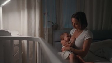 Genç güzel annem, emzirme gece, onun yeni doğan bebek çocuk loş ışık. Anne emzirme bebek