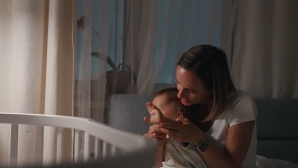 Fiatal anya és baba a bölcsőben éjszaka. A nő odahajolt a gyerekhez, a gyerek odahúzta a kezét. — Stock videók