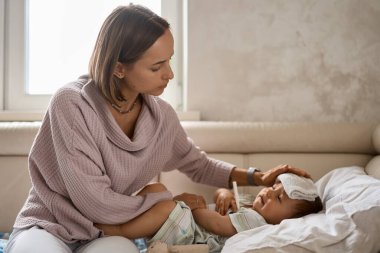 Onun baş ve ölçüm sıcaklığı termometre ile üzerinde soğutucu jel ile genç küçük çocuk kanepede. ve kendine iyi bak onu anne tarafından