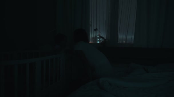 Foto nocturna de una madre despertando por la noche con un bebé llorando en la cuna infantil. Niño neonato caucásico en casa en dormitorio para niños. Concepto de la niñez, nueva vida y paternidad — Vídeos de Stock