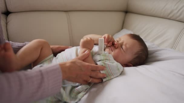 Madre midiendo la temperatura de su hijo enfermo en el fondo. Niño enfermo con fiebre alta acostado en el sofá en casa . — Vídeo de stock