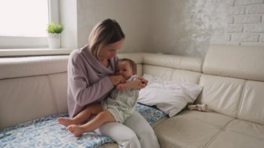 Endişeli genç anne, hasta oğlunun yanında, yüksek ateşi olan kanepede oturuyor. Annem evde battaniyenin altında yatan hasta çocuğun termometresini kullanarak sıcaklık ölçer.