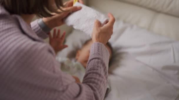 Kleiner Junge auf dem Sofa mit kühlerem Gel auf dem Kopf und Temperaturmessung mit dem Thermometer. und kümmern sich um ihre Mutter — Stockvideo