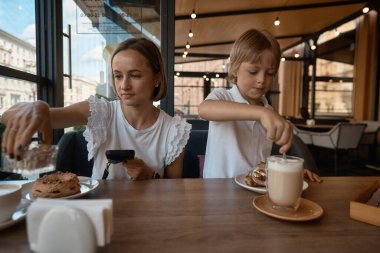 Anne ve oğlu kaldırım restoranında yemek yiyorlar. Anne ve oğul bir kafede kruvasan yiyorlar.