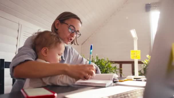 Een jonge moeder werkt thuis met de computer terwijl ze voor haar baby zorgt. Werken vanuit huis tijdens lockdown — Stockvideo