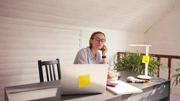 Mulher escrevendo notas falando no celular trabalho remoto do escritório em casa durante o bloqueio vívido — Vídeo de Stock
