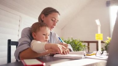 Genç bir anne bebeğiyle ilgilenirken evde bilgisayar kullanarak çalışıyor. Kilitleme sırasında evden çalış