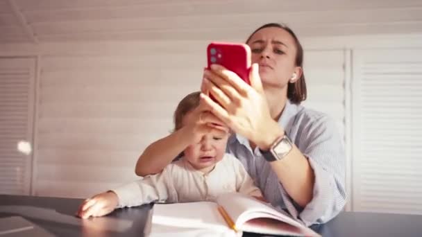 Egy fiatal anya otthon dolgozik, számítógépet használ, miközben vigyáz a babájára. Otthoni munka lezárás alatt — Stock videók