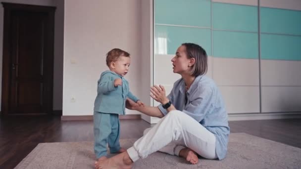 Belle biy bébé caucasien apprenant à marcher en faisant un premier pas à pied à sa mère à la maison. Bébé garçon marchant sur le sol avec pieds nus. Bébé garçon mignon apprenant à marcher. Premiers pas bébé — Video