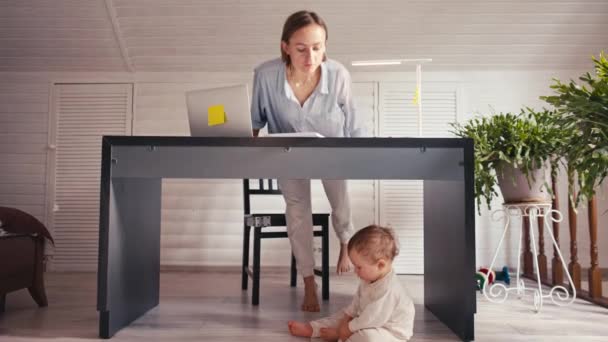 Una joven madre está trabajando en casa usando la computadora mientras cuida a su bebé. Trabajo desde casa durante el encierro — Vídeos de Stock