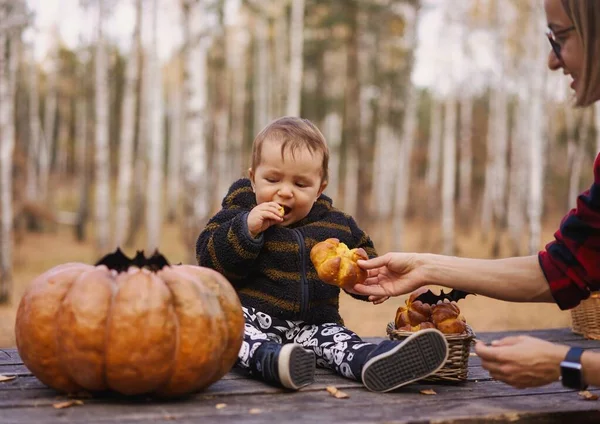 Mujer joven y su hijo bebé en el parque de otoño, niño jugando con la calabaza de Halloween y comer bollo de calabaza. — Foto de Stock