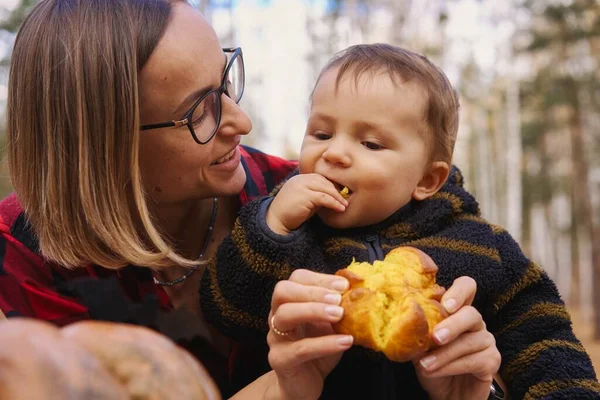 Giovane donna e il suo bambino nel parco autunnale, ragazzo che gioca con la zucca helloween e mangia zucca panino. — Foto Stock