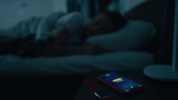 La joven durmiente se despierta temprano en la mañana para desactivar la alarma de smartphone activada en la mesita de noche. Despierta para correr. Fotografía cinematográfica — Vídeo de stock