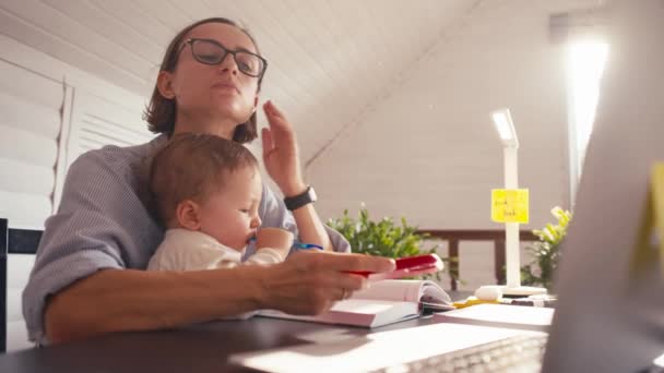 Μια νεαρή μητέρα εργάζεται στο σπίτι χρησιμοποιώντας υπολογιστή, ενώ αυτή φροντίζει το μωρό της. Εργασία από το σπίτι κατά τη διάρκεια αποκλεισμού — Αρχείο Βίντεο
